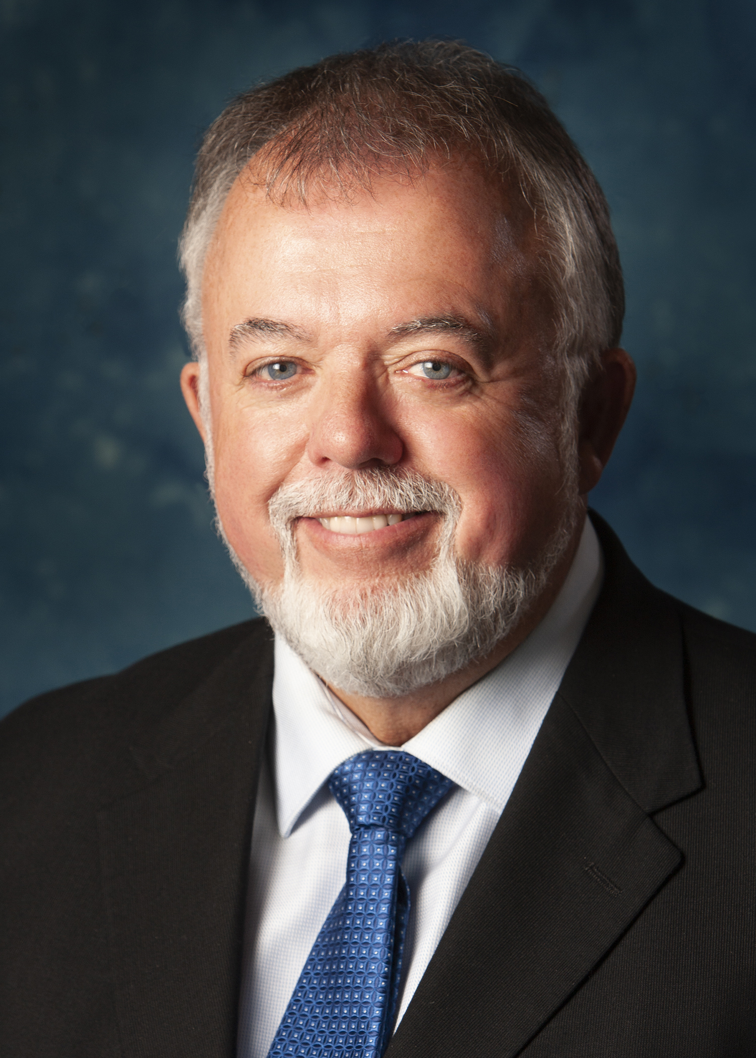 Headshot of a man with a mustache and bearding wearing a tie and suit jacket
