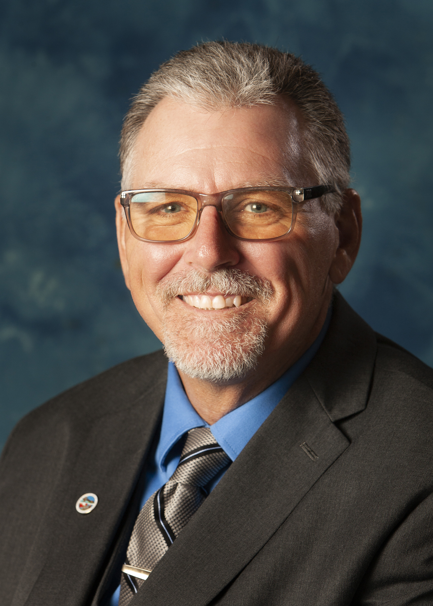 Headshot of man with glasses wearing a tie and suit jacket