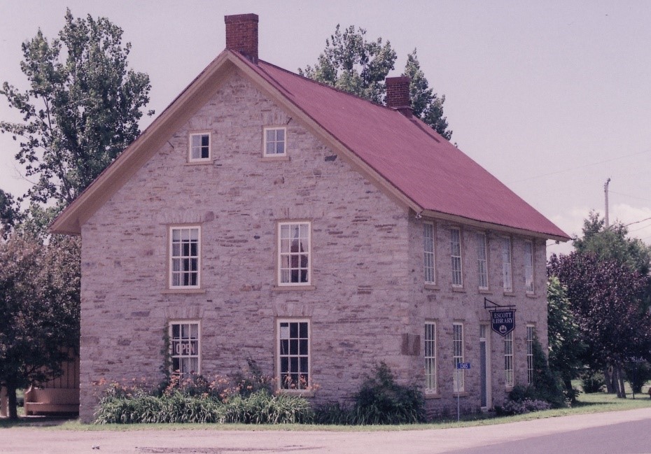 Side view of a stone two story house with oblong windows and a red roof
