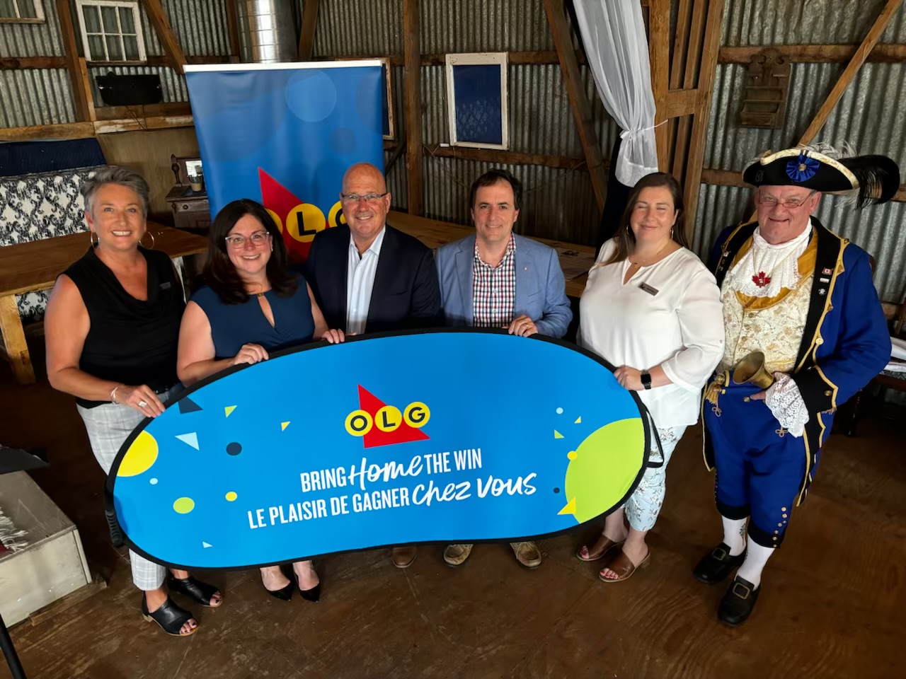 Group Shot of OLG, local MPP,Mayors and Town Crier behind a sign